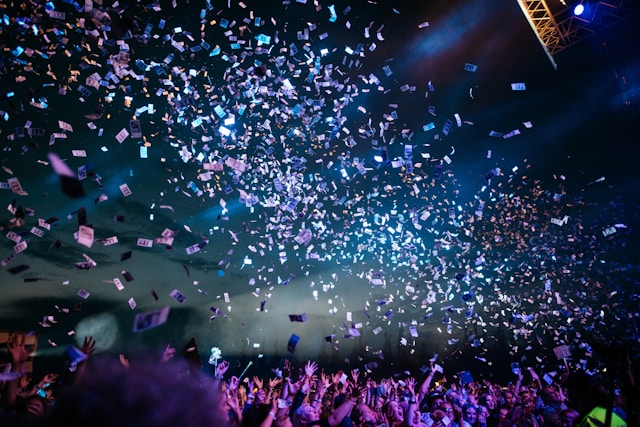 A vibrant crowd at a live event with colorful confetti raining down under bright stage lights, capturing the excitement and engagement of the audience.