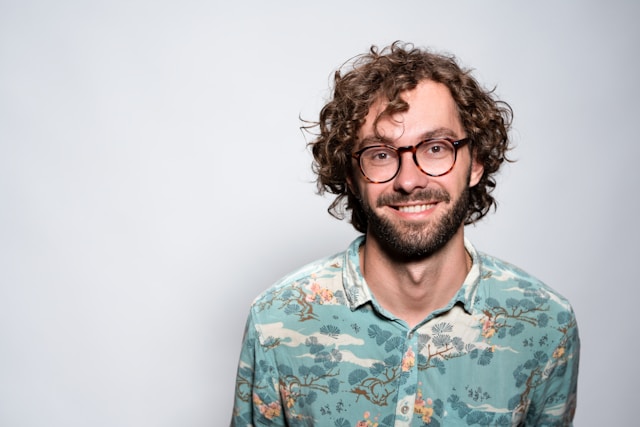 Young man with glasses smiling during a casual professional headshot.